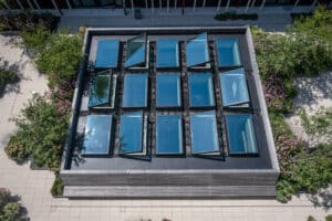 Lamilux zeigt eine Dachterrasse mit einzelnen rechteckigen Dachfenstern, die in einem Quadrat angeordnet und teilweise geöffnet sind.