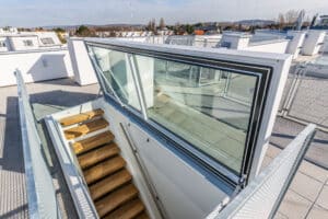 Lamilux zeigt eine Dachterrasse, die über einen Treppenaufgang und ein großes Dachfenstern erreicht werden kann.