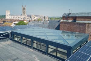 Lamilux zeigt eine große Glasdachfläche, die in Quadrate unterteilt ist, mit senkrechten Fenstern auf einem Flachdach.