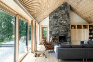 Wohnraum mit toller Aussicht, Terrasse, gemauertem Kamin, Hebeschiebetüren mit hellem Holzrahmen und passender Holzsprossendecke in der Dachschräge von M Sora Fenster.