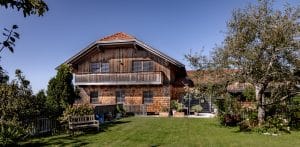 Newo Sonnen- und Insektenschutz zeigt ein Holzhaus dessen Fenster und Terrassentüren mit Raffstore beschattet werden.