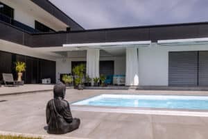 Ein Poolbereich in Frontalansicht mit elektrischer Markise in Weiß-Grau und passendem Textilvorhang, der Schatten spendet und das Terrassenambiente ergänzt von Newo.