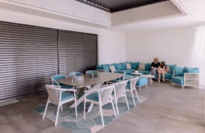 Eine Terrassenschiebetür mit schwarzem Alu-Rahmen und außenliegenden, dunkelgrauen, geschlossenen Raffstores, davor eine XXL-Outdoorlounge mit großflächigen Bodenfliesen von Newo.