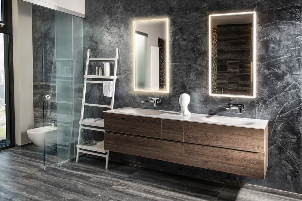Modernes barrierefreies Badezimmer mit schwebendem Waschtisch aus dunklem Holz und Wand und Bodengestaltung in dunkler Schiefer- und Steinoptik mit einer Glas-Schiebetür im WC-Bereich von HOLTER gezeigt von Limbach.