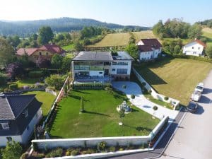 Villa mit Flachdach, dachmontierten Solarpaneelen, überdachter Terrasse und einem großzügigem Vorgarten mit Brunnen aus der Vogelperspektive von Planungsbüro Schaufler.