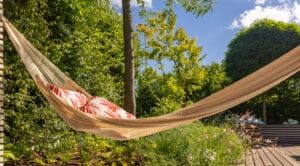 Eine gemütliche Terrasse mit einer schwebenden Hängematte zwischen zwei Gestellen, umgeben von üppigem Grün von Prachtgarten.