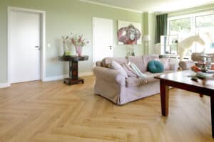 Ein modernes Wohnzimmer mit elegantem Fischgrätboden in natürlicher Holzoptik, hellen Wänden und stilvoller Einrichtung – von Project Floors.