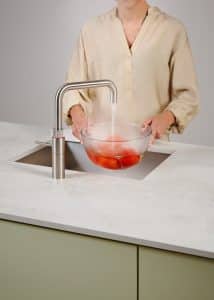 Eine Frau blanchiert Tomaten mit dem kochenden Wasser der Armatur Fusion Square aus rostfreiem Stahl von Quooker.