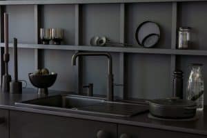Eine komplett in Schwarz gehaltene moderne Küchenzeile mit Regalrückwand, passenden Küchenutensilien, einer quadratischen Spüle mit Ablage und einer Quooker Fusion Square-Armatur in Schwarz mit passendem Einbau-Seifenspender.