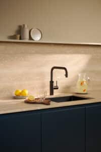 Ein “Quooker Flex Square”-Wasserhahn in Gunmetal in einer beige‑marineblauen Küche mit flexiblem Auslauf und modernem Design von Quooker.