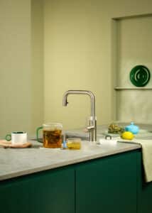 Ein “Quooker Flex Square”-Wasserhahn in rostfreiem Volledelstahl in einer in Grüntönen gehaltenen Küche von Quooker.