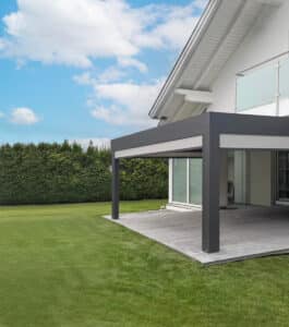 Ein Haus mit anthrazitfarbener Pergola und geöffneten hellgrauen Senkrechtmarkisen über einer Holzterrasse von Sonnenschutz Rachbauer.