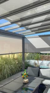 Ein Sommergarten bzw. Pergola mit Outdoorlounge, Glasdach und Senkrechtmarkisen umgeben von einem wilden, blühenden Garten von Sonnenschutz Rachbauer.