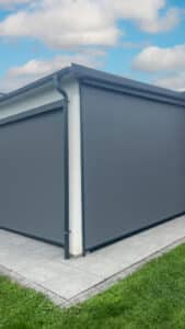 Ein Haus mit einer gemauerten Terrasse und seitlich geschlossenen schwarzen Anthrazit‑Seitenmarkisen als funktionaler Sicht‑ und Sonnenschutz von Sonnenschutz Rachbauer.
