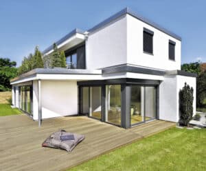 Einfamilienhaus mit Flachdach, halbüberdachter Eckterrasse mit Terrassenschiebetüren, zweitem Terrassenzugang, Holzdielenterrasse und einer Dachterrasse im Obergeschoß von Regnauer Fertighaus.