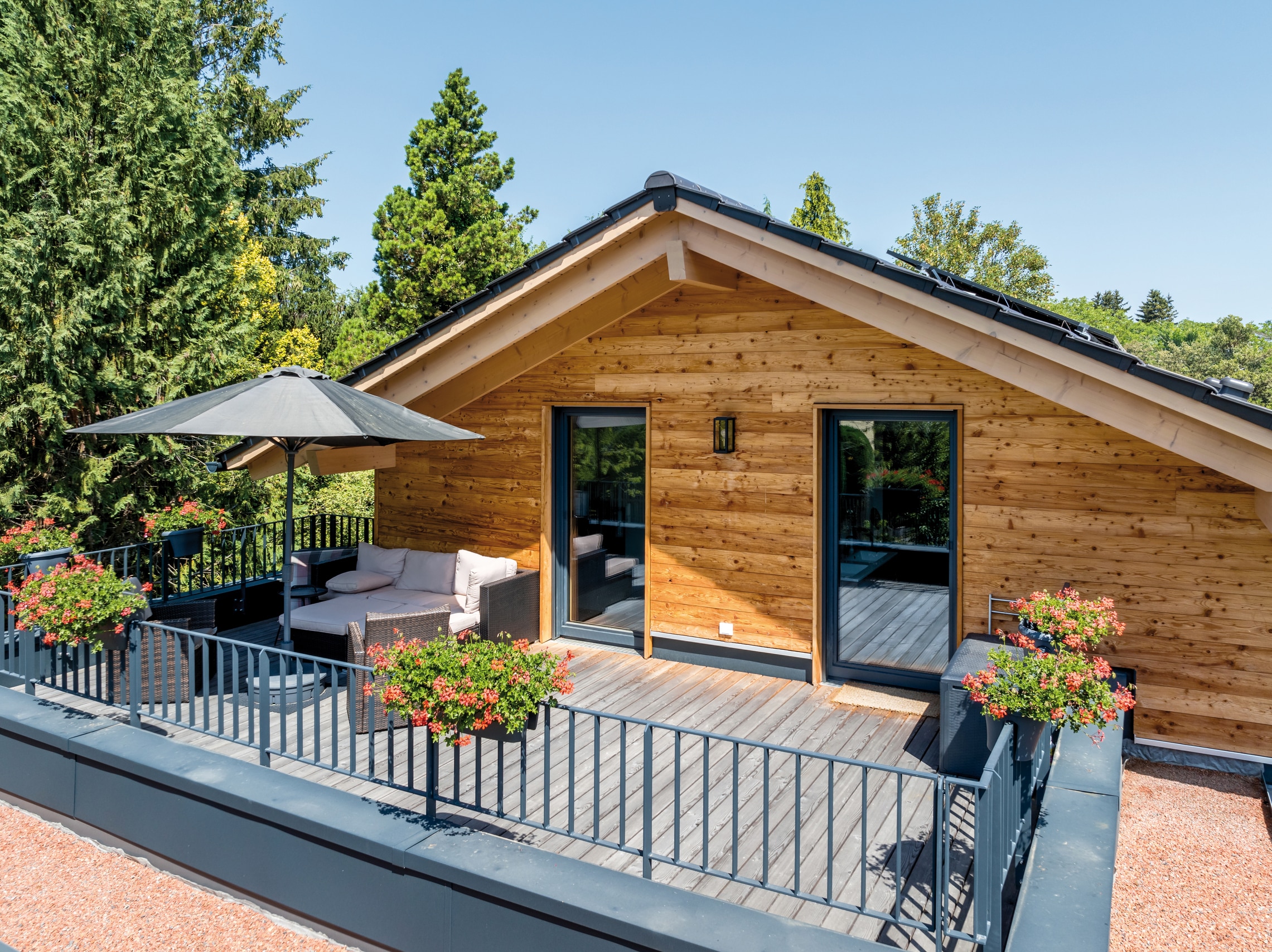 Regnauer Fertighaus zeigt große Terrasse mit dunkelgrauem Geländer eines modernen Holzhaus mit Satteldach.