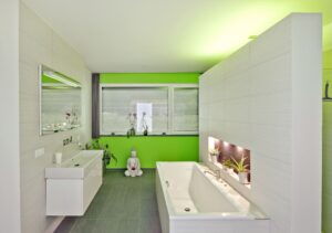 Ein Badezimmer mit wandhohen Fliesen, einem schwebenden Doppelwaschtisch, Badewanne, gefliester Trennwand zur Dusche, WC-Nische, leuchtend grüner Akzentwand und Fensterfront mit Außenjalousie von Regnauer.