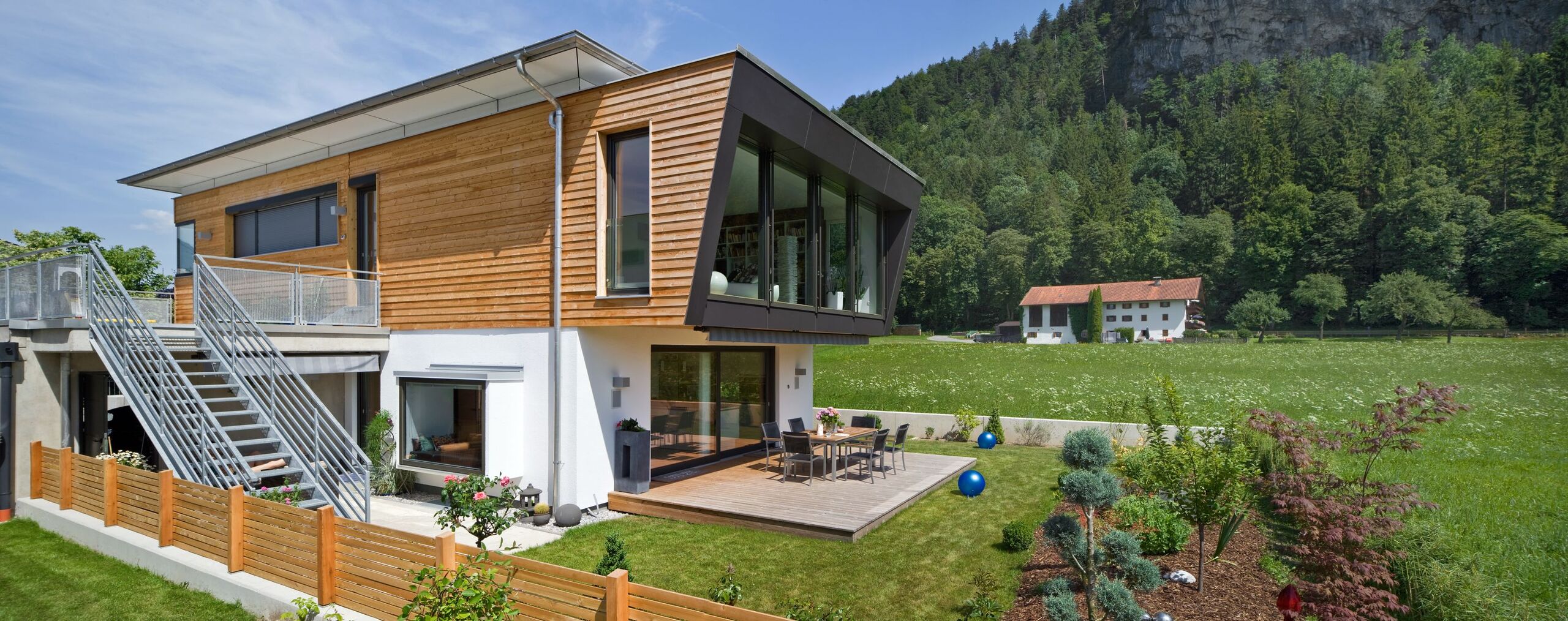 Eine moderne Villa mit schlanker Seitenansicht, Holzverkleidung, großen Fensterflächen und einem gepflegten Garten von Regnauer.