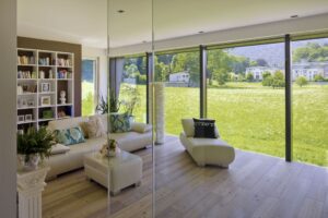 Ein Wohnzimmer mit großer Glasfront und bodentiefen Fenstern, die in den grünen Garten zeigen von Regnauer.