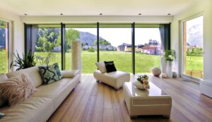 Ein Wohnzimmer mit dreiseitiger Festverglasung, beidseitigen Terrassentüren und einer hochwertigen Ledercouch mit Pouf und Chaiselongue von Regnauer.