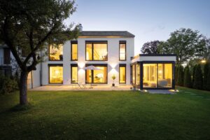 Ein modernes Haus bei Nacht mit angestückeltem Wintergarten, bodentiefen Fenstern mit schwarzem Rahmen, Schiebetüren und französischem Balkon von Regnauer.