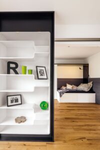 Ein heller Arbeits-/Gäste-/Jugendraum mit ausziehbarem Couchbett und raumtrennendem Regalelement von Regnauer.