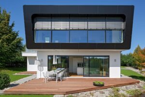 Ein modernes Einfamilienhaus bodentiefen Fensterflächen, Außenjalousien und einer überdachten Terrasse mit Deckenleuchten von Regnauer.