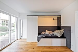 Ein helles Gäste- bzw. Jugendzimmer mit wandlaufender Schiebetür und bodentiefer Terrassenschiebetür, das zugleich Durchgangszimmer ist von Regnauer.