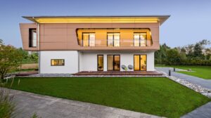 Eine moderne kubische Villa mit seitlicher Terrasse unter Dach, Loggia mit Glasgeländer, auskragendem Dachvorsprung und Fassadenelementen in Holzoptik von Regnauer.