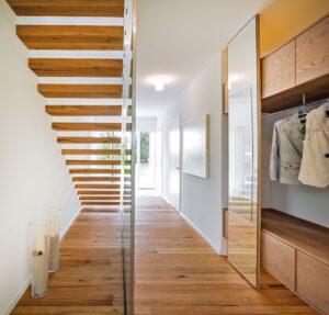 Ein heller Vorraum mit Garderobe, einer modernen Kragarmtreppe mit schwebenden Stufen und Glasgeländer sowie eine Schiebetür, die in den Wohnbereich führt von Regnauer.