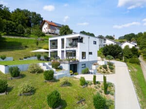 Ein mehrstöckiges Regnauer Fertighaus am Hang mi Außenaufgang zum Garten und Hauseingang mit integrierter Garageneinfahrt Regnauer Hausbau.