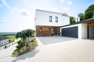 Ein überdachter Hauseingang mit angeschlossener Garage und Holzfassade in einem hanggebauten Fertighaus von Regnauer Hausbau.