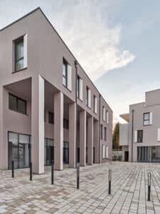 RÖFIX präsentiert die Außenansicht des Referenzprojekts Stadthaus Lederergasse mit Flachdach, grauem Außenputz und modernen Säulen.