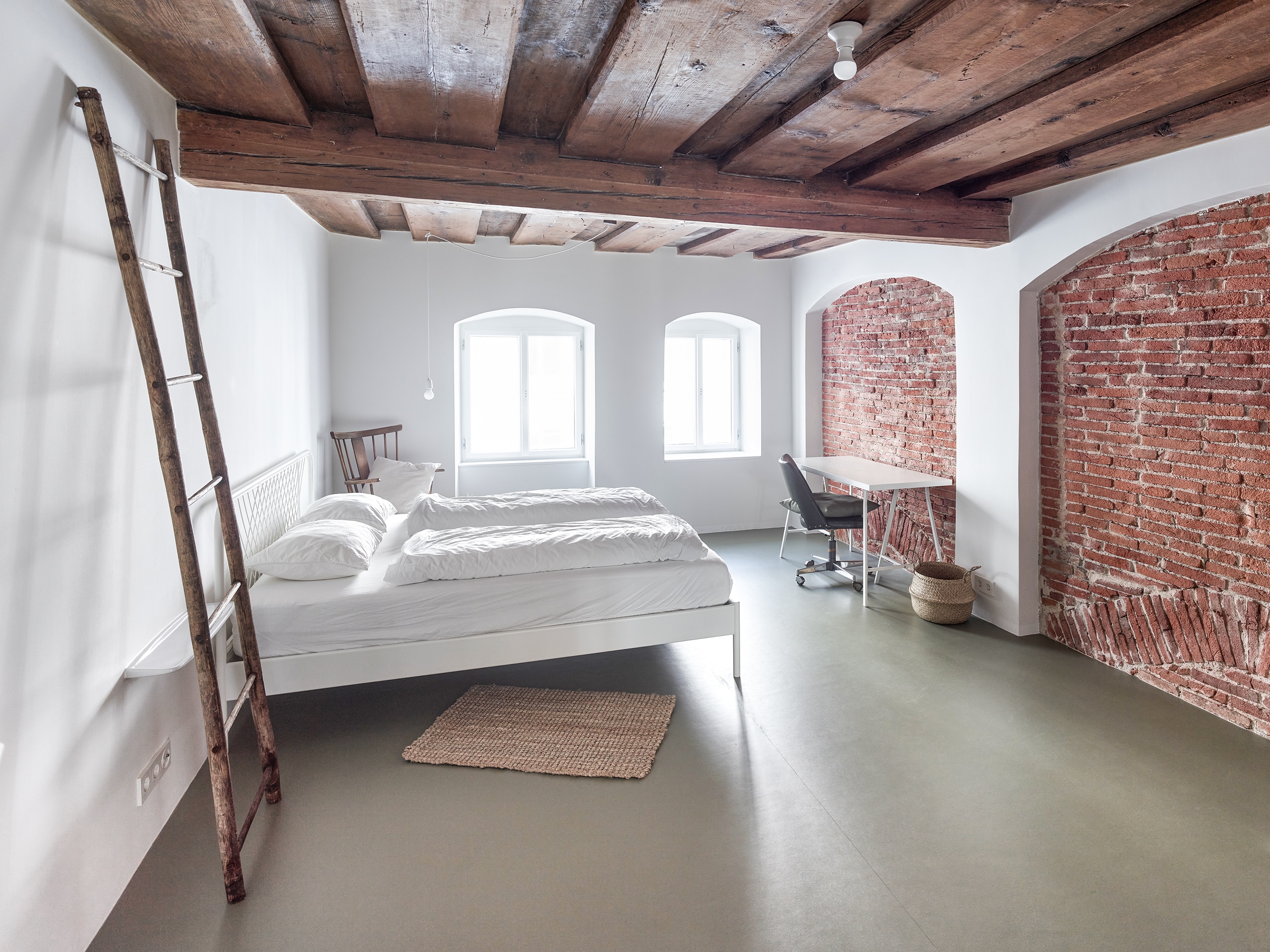 RÖFIX präsentiert ein Schlafzimmer das Referenzprojekt Stadthaus Lederergasse mit Holzdecke und zwei mit Ziegelwand verbauten Gewölbebögen.