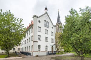 RÖFIX präsentiert die Außenansicht eines Klosters als Referenzprojekt mit Satteldach, kleinem Türmchen und kantigen Säulen an den Hausecken.