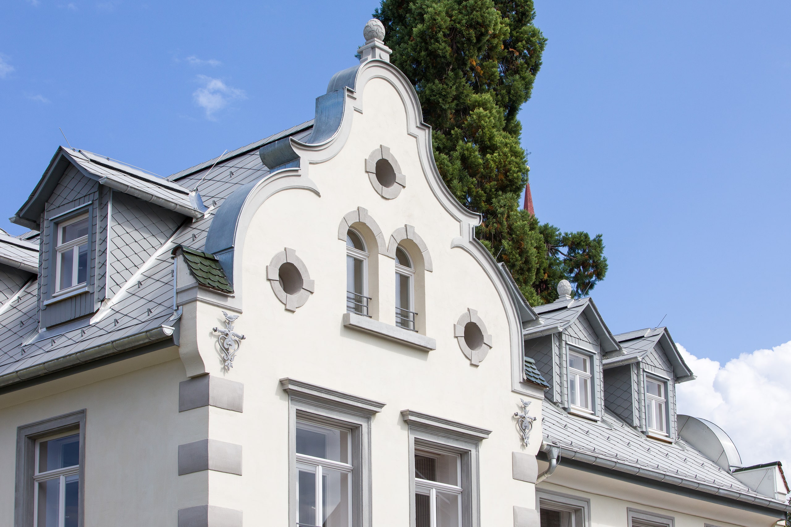 RÖFIX zeigt die Außenansicht einer renovierten Villa mit Satteldach und weißem Außenputz mit Verziehrungen.