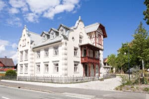 RÖFIX zeigt die Außenansicht einer renovierten Villa mit Satteldach, Fachwerkaufbau und weißem Außenputz mit Verziehrungen.