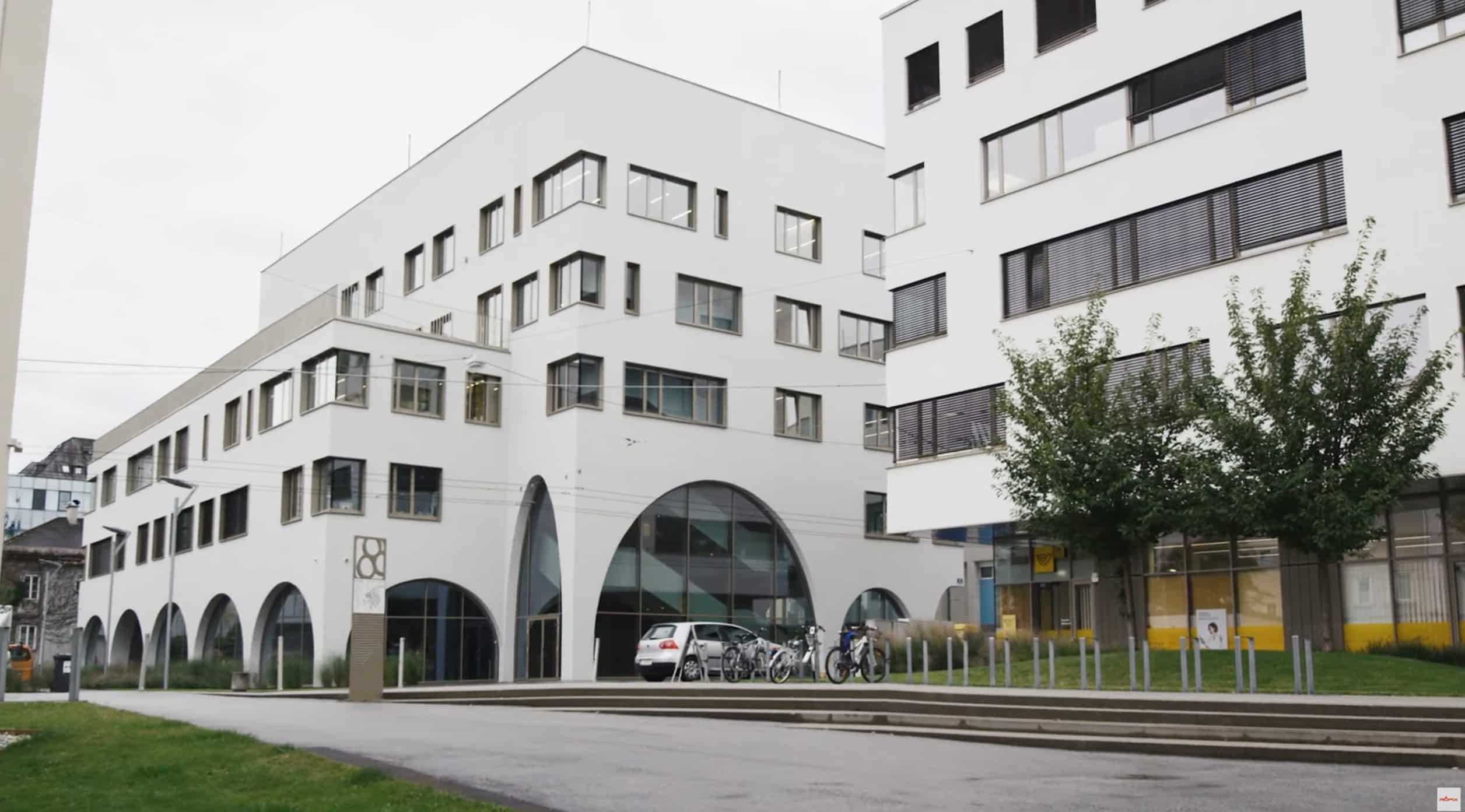 RÖFIX zeigt das Referenzprojekt PMU Salzburg mit weißer Fassade, Flachdach, Terrasse und Rundbögen.