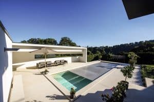 RUHA präsentiert eine Terrasse mit großen beigen Fliesen, einem Pool, einer Lounge und Bepflanzung.