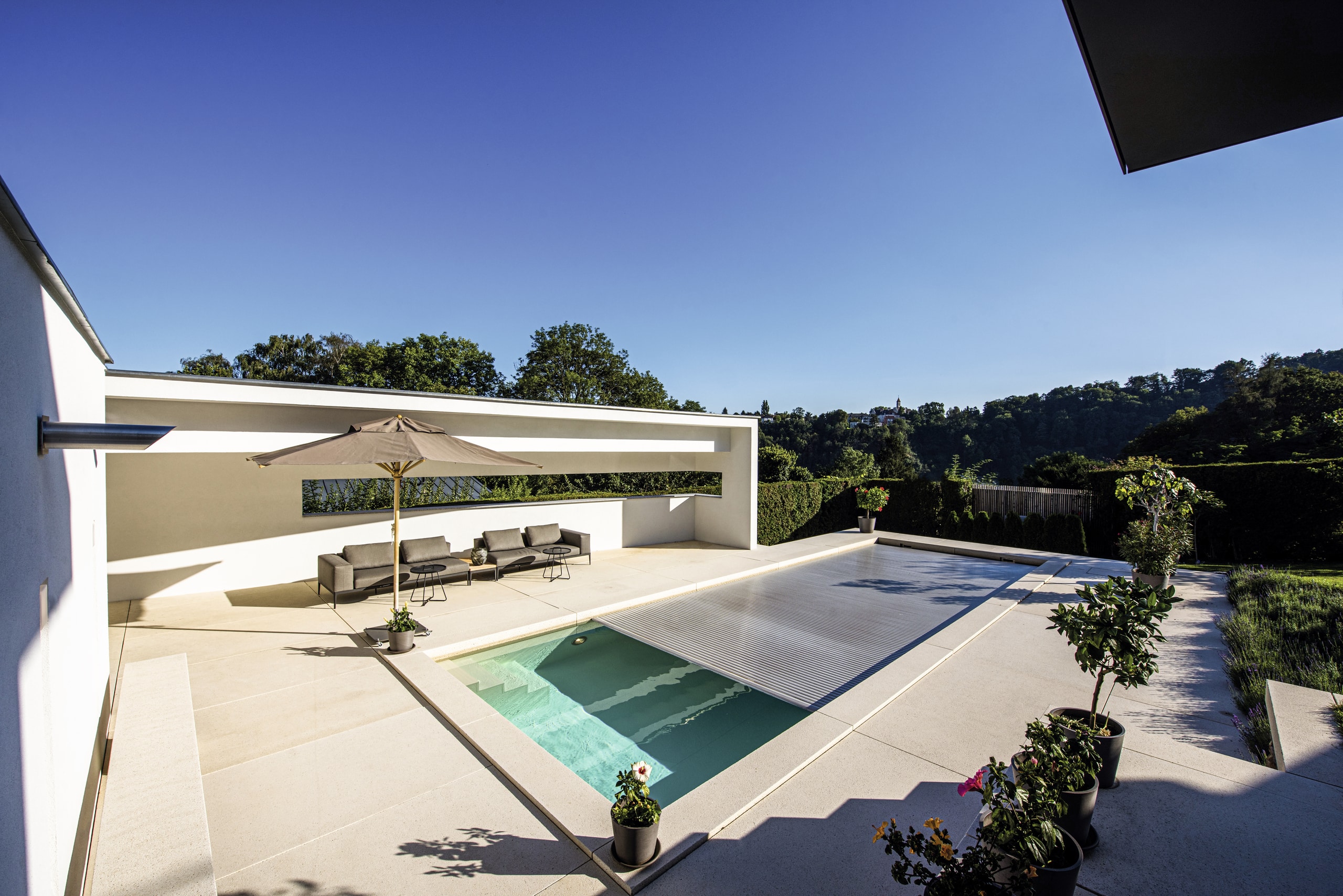 RUHA präsentiert eine Terrasse mit großen beigen Fliesen, einem Pool, einer Lounge und Bepflanzung.