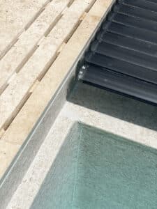 Eine Nahaufnahme einer Infinity‑Poolkante mit Überlaufrinne, Fliesenrand und schwarzer Poolabdeckung von Ruha Stelzmüller.