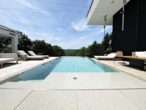 Eine Infinity-Poolkante mit Überlaufrinne, Fliesenrand, Relaxliege und barrierefreiem Einstieg von Ruha Stelzmüller.