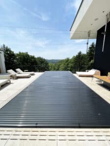 Ein Infinity‑Pool mit Überlaufrinne, Fliesenumrandung und Relaxliege, umgeben von einem Terrassengeländer in schwarzer Sprossenoptik und mit schwarzer Poolabdeckung von Ruha Stelzmüller.