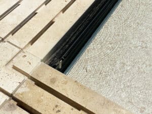 Nahaufnahme einer Poolumrandung mit Ablaufrinne und eingezogener schwarzer Poolabdeckung von Ruha Stelzmüller.