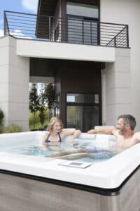 Ruha Stelzmüller zeigt ein Whirlpool, das auf einer Terrasse vor einem modernen Haus im Freien steht und außen mit Holz verkleidet ist.