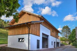 Heizhaus mit Sattel- und Pultdach, Fassadenmix aus Holz und Putz, zwei Garagen-Sektionaltoren und Hackgutlager von SCE Reisinger Bau.