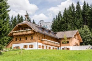 Rustikales Holzhaus mit klassischen Holzsprossenfenstern mit Fensterläden, Walmdach, Walmgauben und zwei Holzbalkonen von SILBER Fensterbau.
