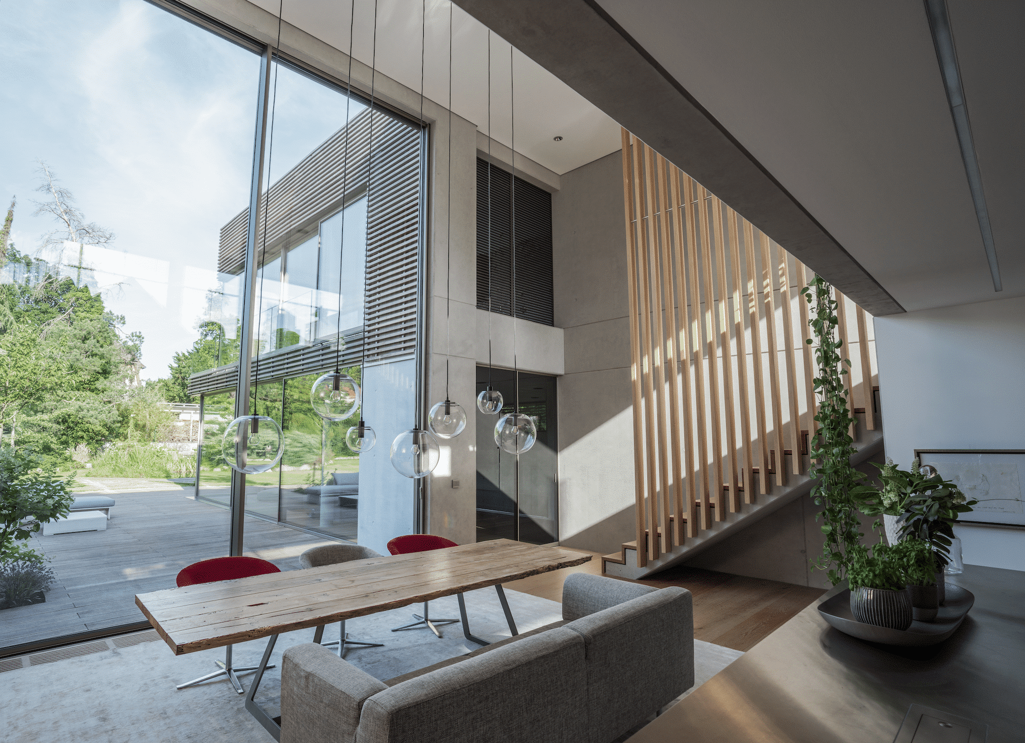 Solarlux zeigt modernen offenen Wohnraum mit Stiegenaufgang und raumhoher Glasfront und Glasschiebetür.