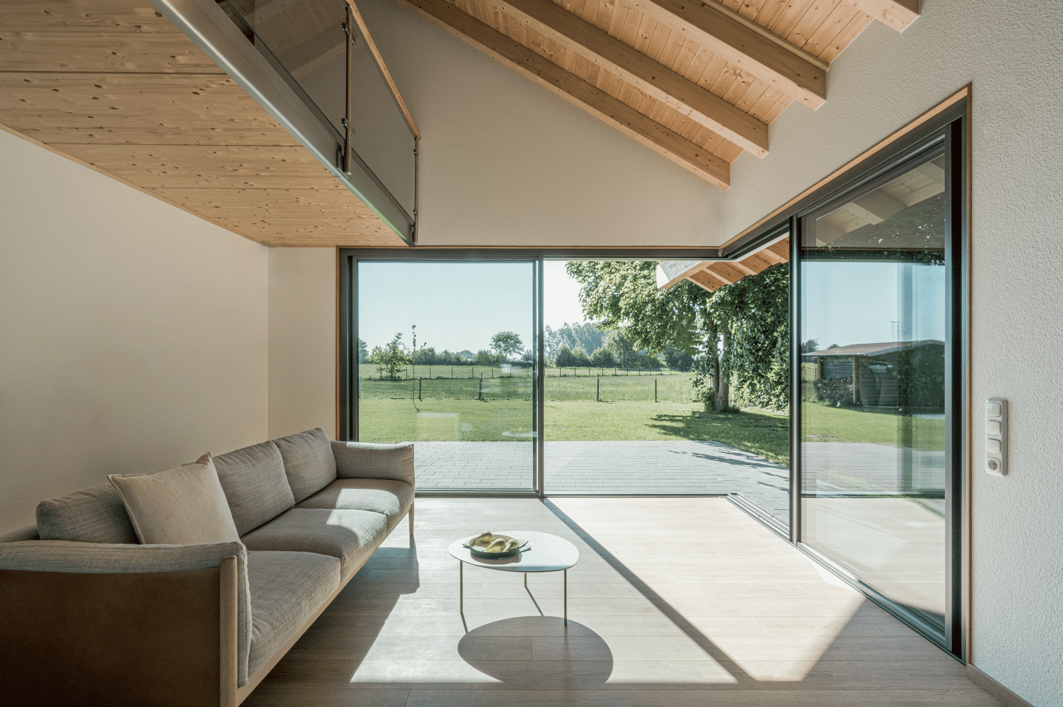 Solarlux zeigt einen Wintergarten mit einer grauen Couch und einem kleinen Beistelltisch mit Zugang zum Garten durch ein Schiebefenster.