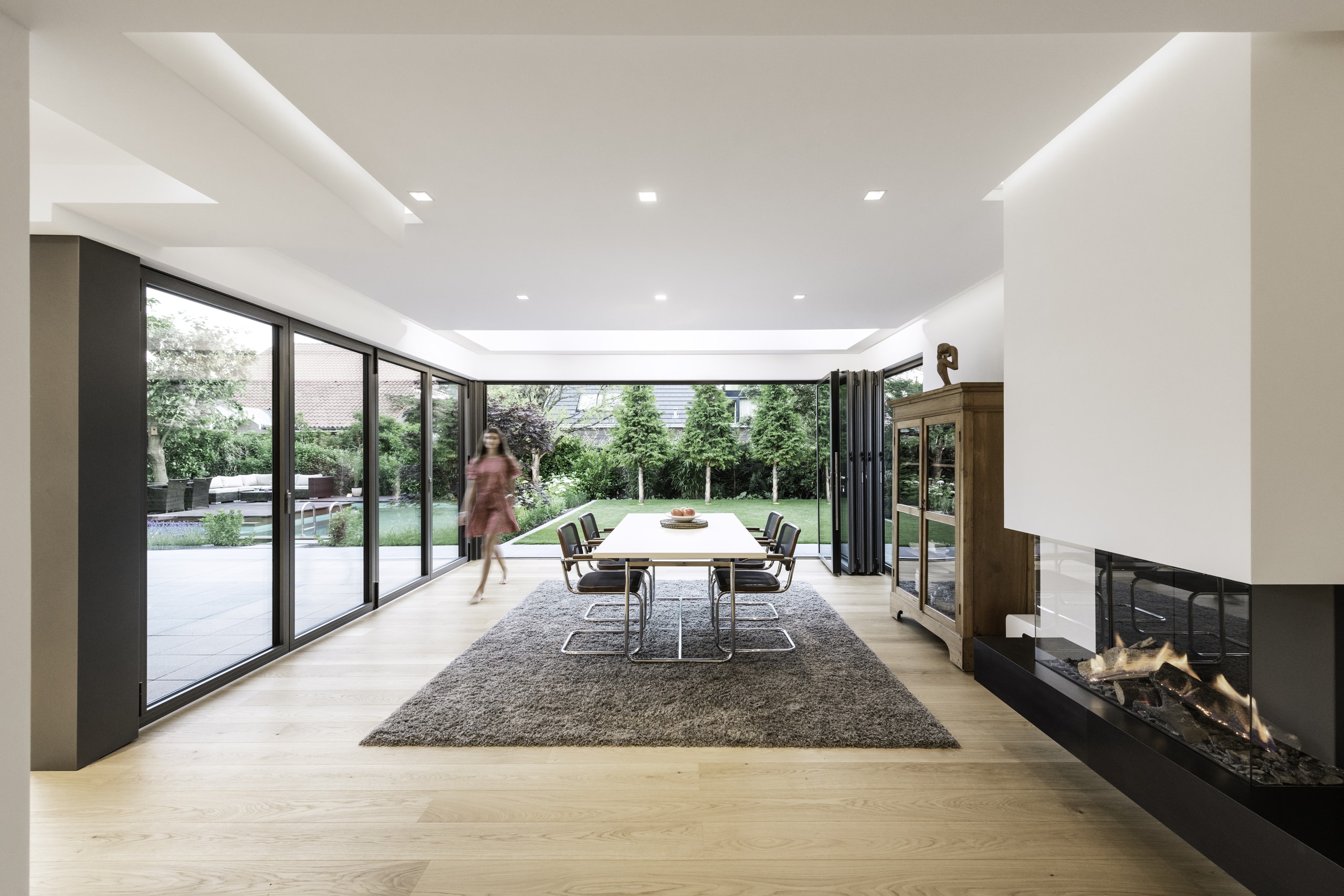 Solarlux zeigt großes Esszimmer mit auf einer Seite zur Gänze geöffneten Faltschiebetür mit dunkelgrauem Rahmen mit Blick auf Garten und Pool.